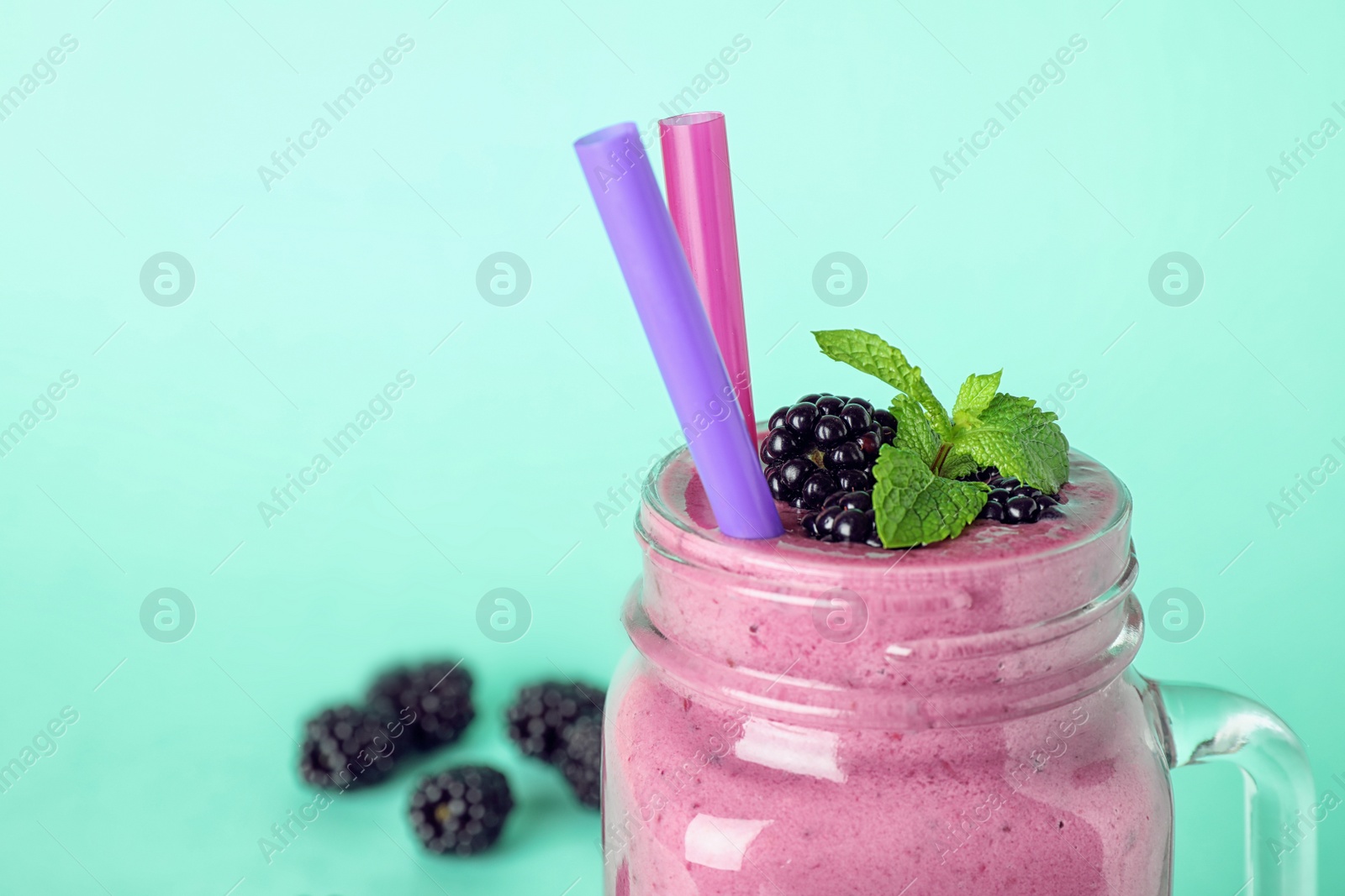 Photo of Mason jar of tasty blackberry smoothie with straws on turquoise background, closeup. Space for text