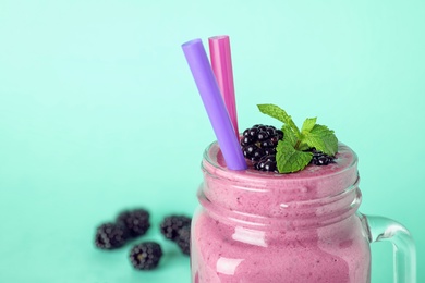 Mason jar of tasty blackberry smoothie with straws on turquoise background, closeup. Space for text