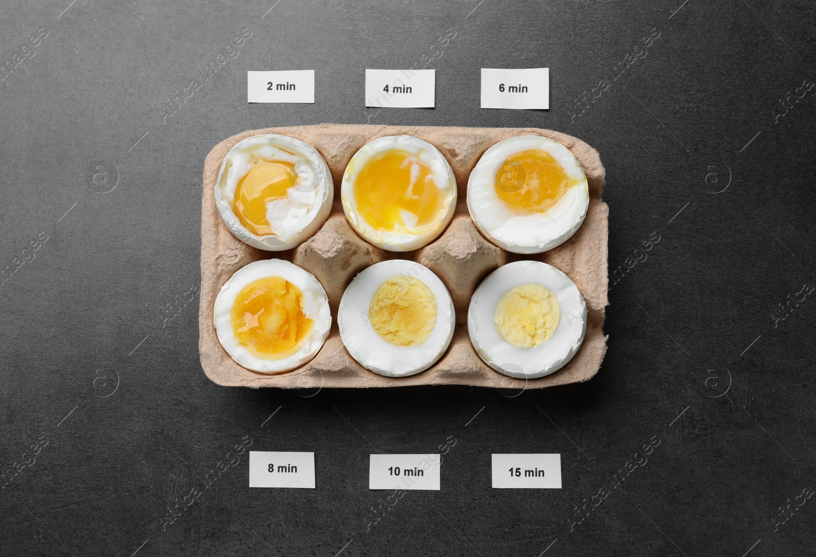 Photo of Different cooking time and readiness stages of boiled chicken eggs on dark grey table, flat lay