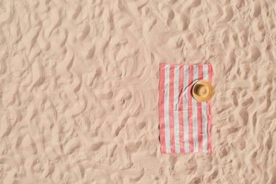 Image of Towel with straw hat on sandy beach, top view. Space for text