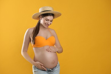 Young pregnant woman wearing swimsuit on yellow background, closeup. Sun protection concept