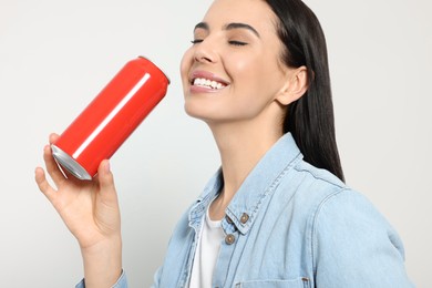 Beautiful happy woman drinking from red beverage can on light grey background