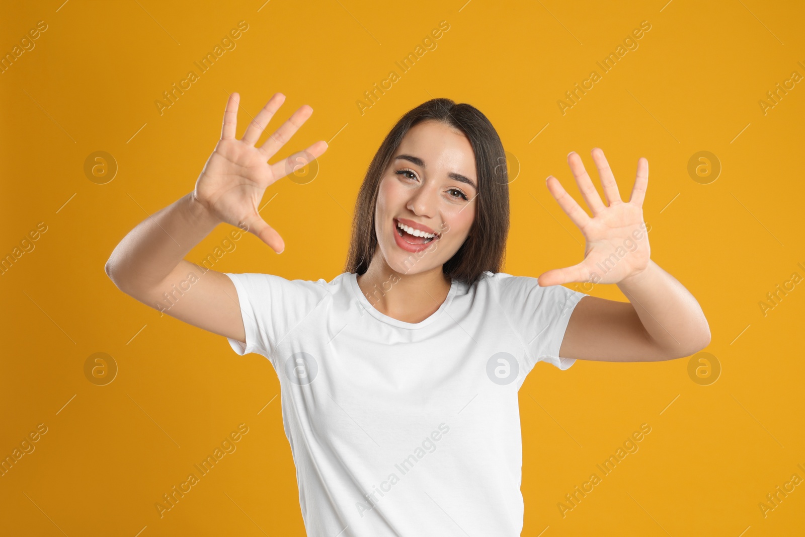 Photo of Woman in white t-shirt showing number ten with her hands on yellow background