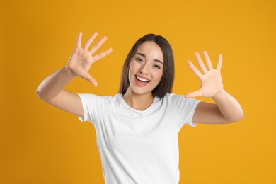 Woman in white t-shirt showing number ten with her hands on yellow background