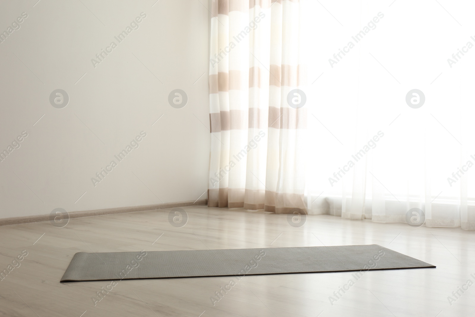 Photo of Unrolled grey yoga mat on floor in room. Space for text