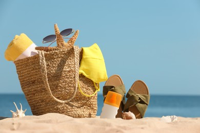 Bag with beach accessories and slippers on sand near sea