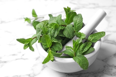 Mortar with fresh green mint and pestle on table, closeup