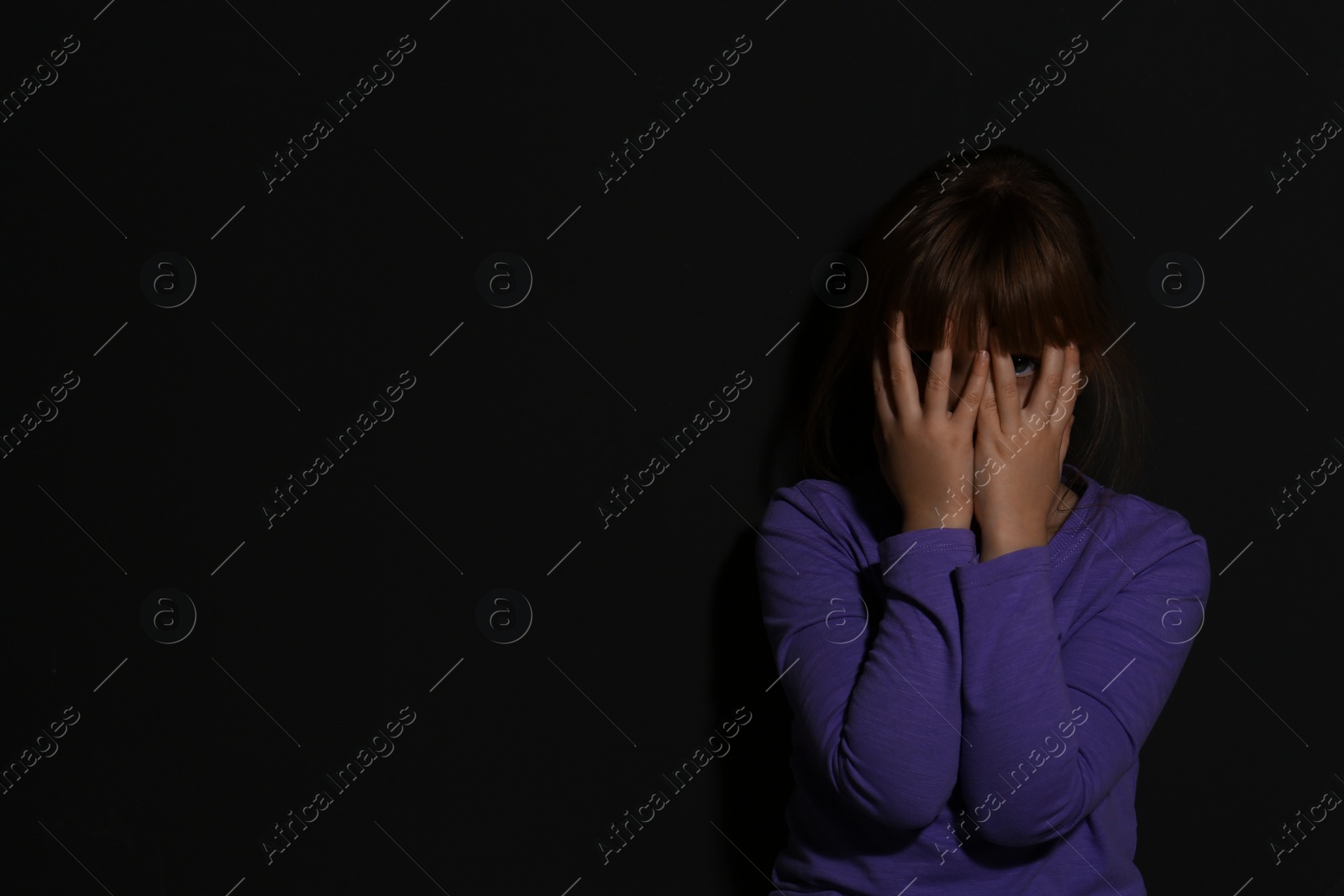 Photo of Abused little girl crying near black wall, space for text. Domestic violence concept
