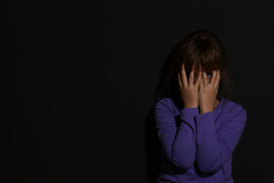Abused little girl crying near black wall, space for text. Domestic violence concept