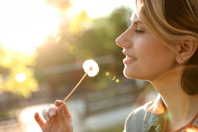 Photo of Young woman with dandelion in park on sunny day. Allergy free concept