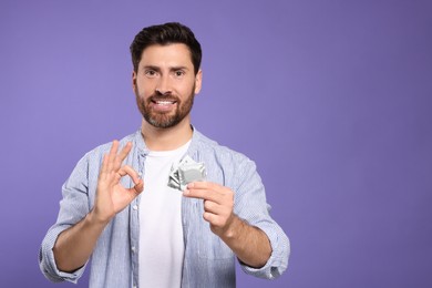 Photo of Man with condoms showing ok gesture on purple background, space for text. Safe sex