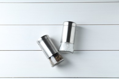 Photo of Salt and pepper shakers on white wooden table, flat lay