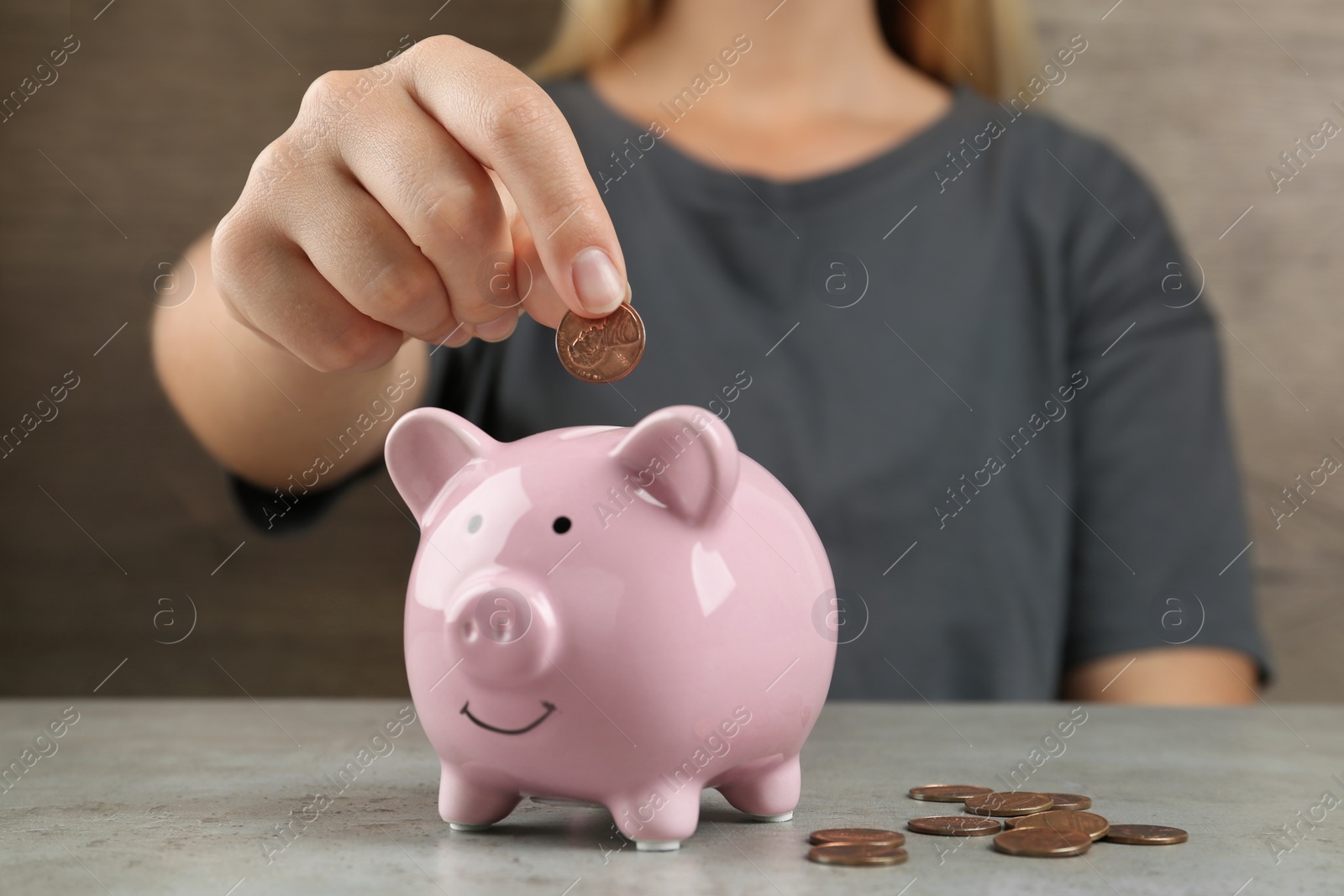 Photo of Woman putting coin into piggy bank on grey stone table, closeup view