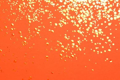 Photo of Shiny bright golden glitter on orange background, flat lay