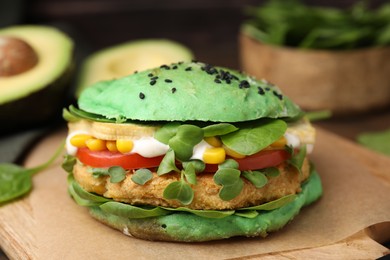 Photo of Tasty green vegan burger with vegetables, patty and microgreens on wooden board, closeup