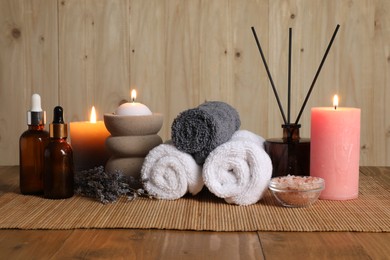 Photo of Aromatherapy. Scented candles, bottles, lavender, towels and sea salt on wooden table