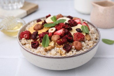 Photo of Oatmeal with freeze dried fruits, nuts and mint on white wooden table, closeup