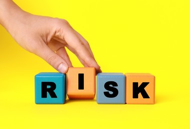 Photo of Woman making word Risk with colorful cubes on yellow background, closeup