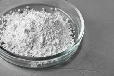 Photo of Petri dish with calcium carbonate powder on grey table, closeup