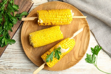 Fresh corn cobs with butter on white wooden table, flat lay