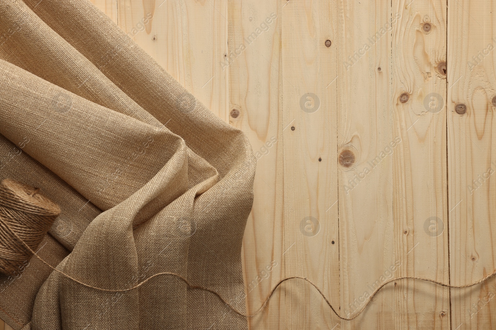 Photo of Burlap fabric and spool of thread on wooden table, top view. Space for text