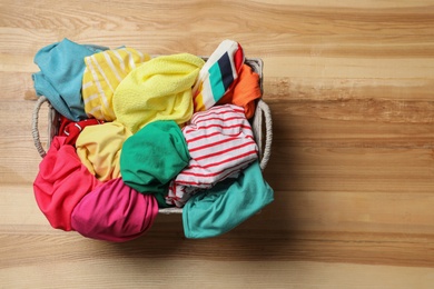 Photo of Wicker basket with laundry on wooden surface, top view