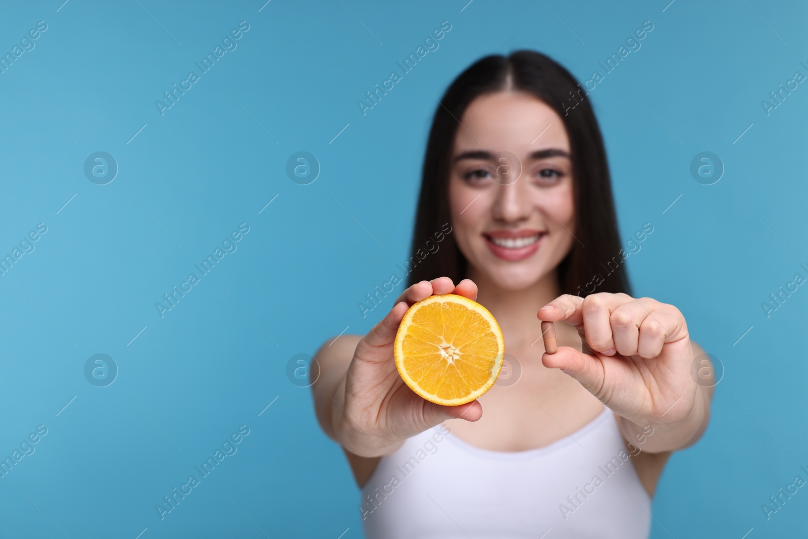 Photo of Beautiful young woman with vitamin pill and piece of orange on light blue background, selective focus. Space for text
