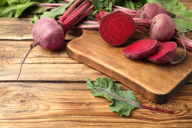 Cut and whole raw beets on wooden table. Space for text