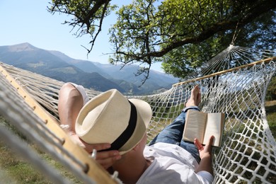 Photo of Young man reading book in hammock outdoors on sunny day