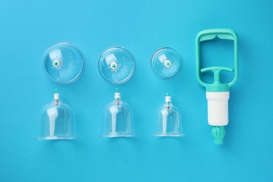 Photo of Plastic cups and hand pump on light blue background, flat lay. Cupping therapy