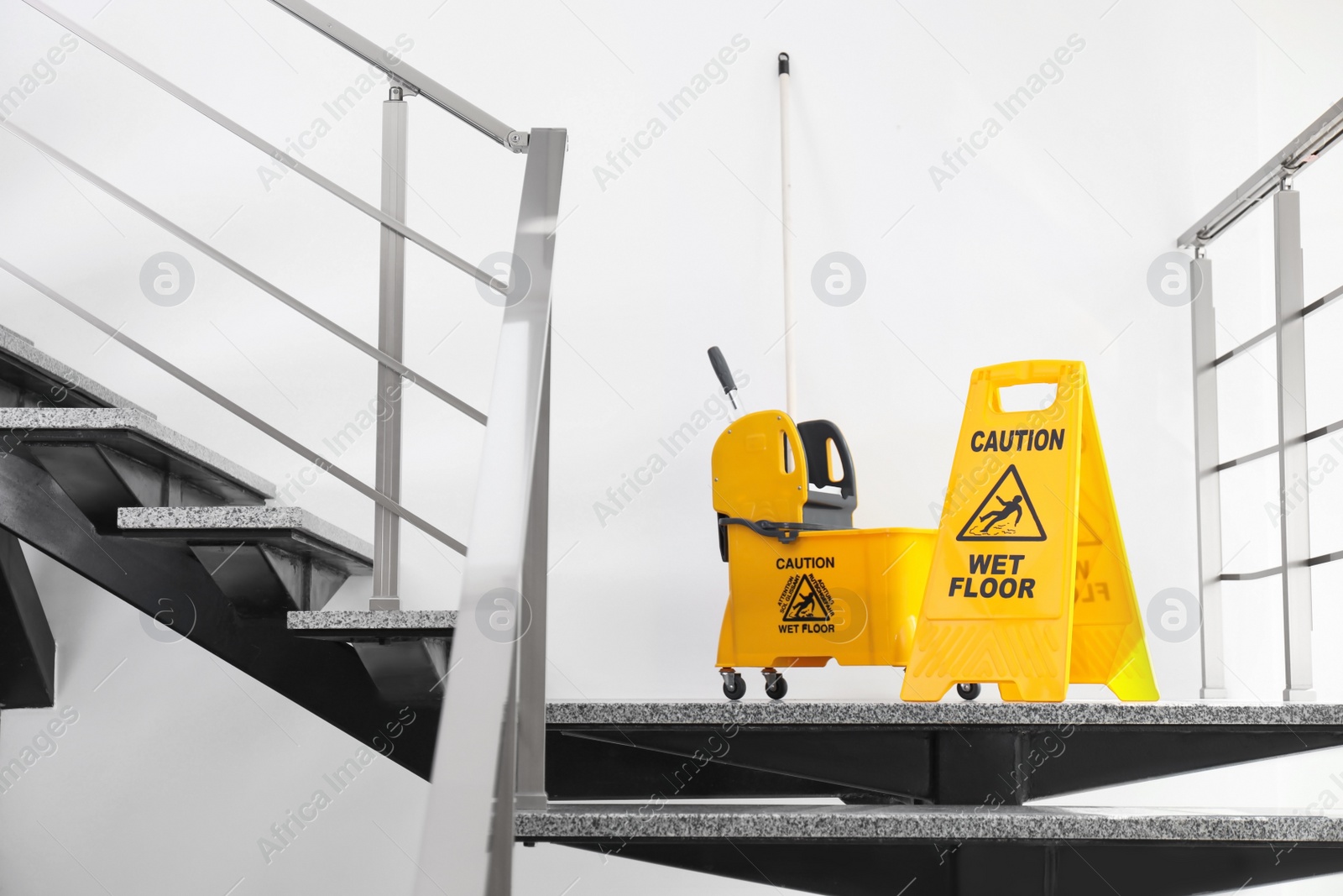 Photo of Safety sign with phrase Caution wet floor and mop bucket on stairs