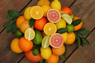 Photo of Different citrus fruits with green leaves on wooden table, flat lay