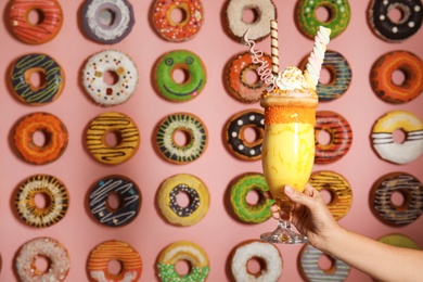 Photo of Woman holding glass of tasty milk shake with sweets near decorated wall, closeup. Space for text