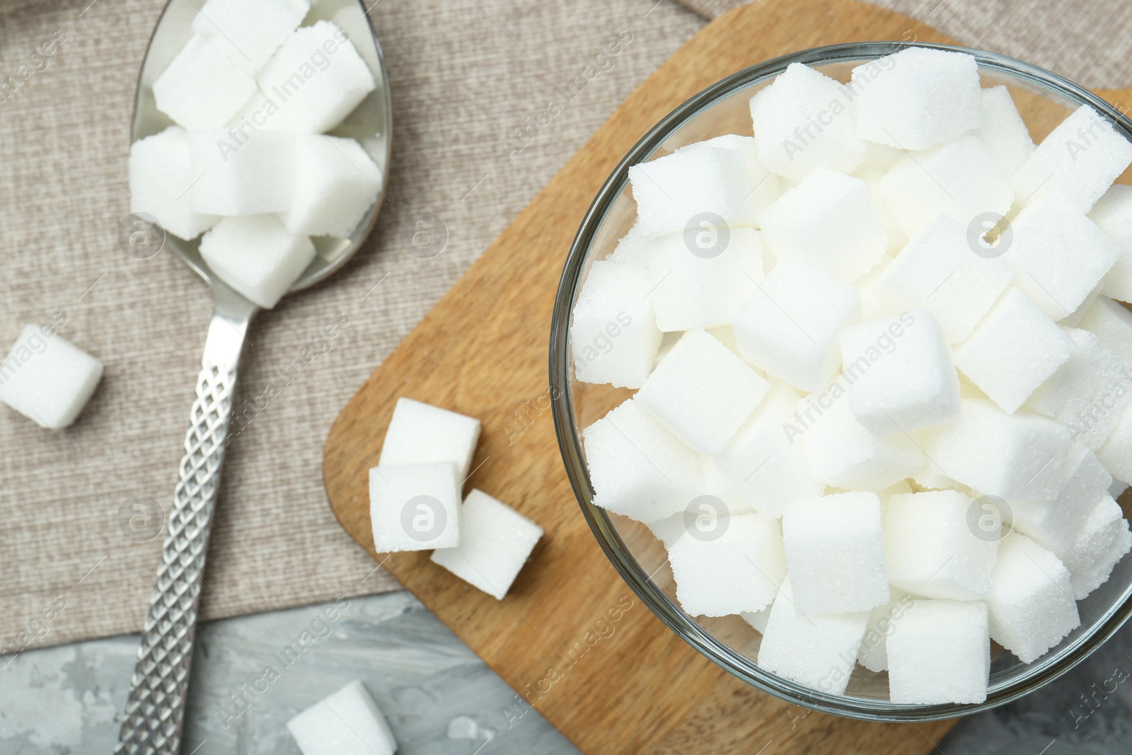 Photo of White sugar cubes in glass bowl on grey table, flat lay