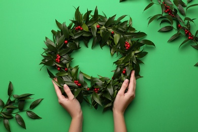 Photo of Woman with beautiful mistletoe wreath on green background, top view. Traditional Christmas decor
