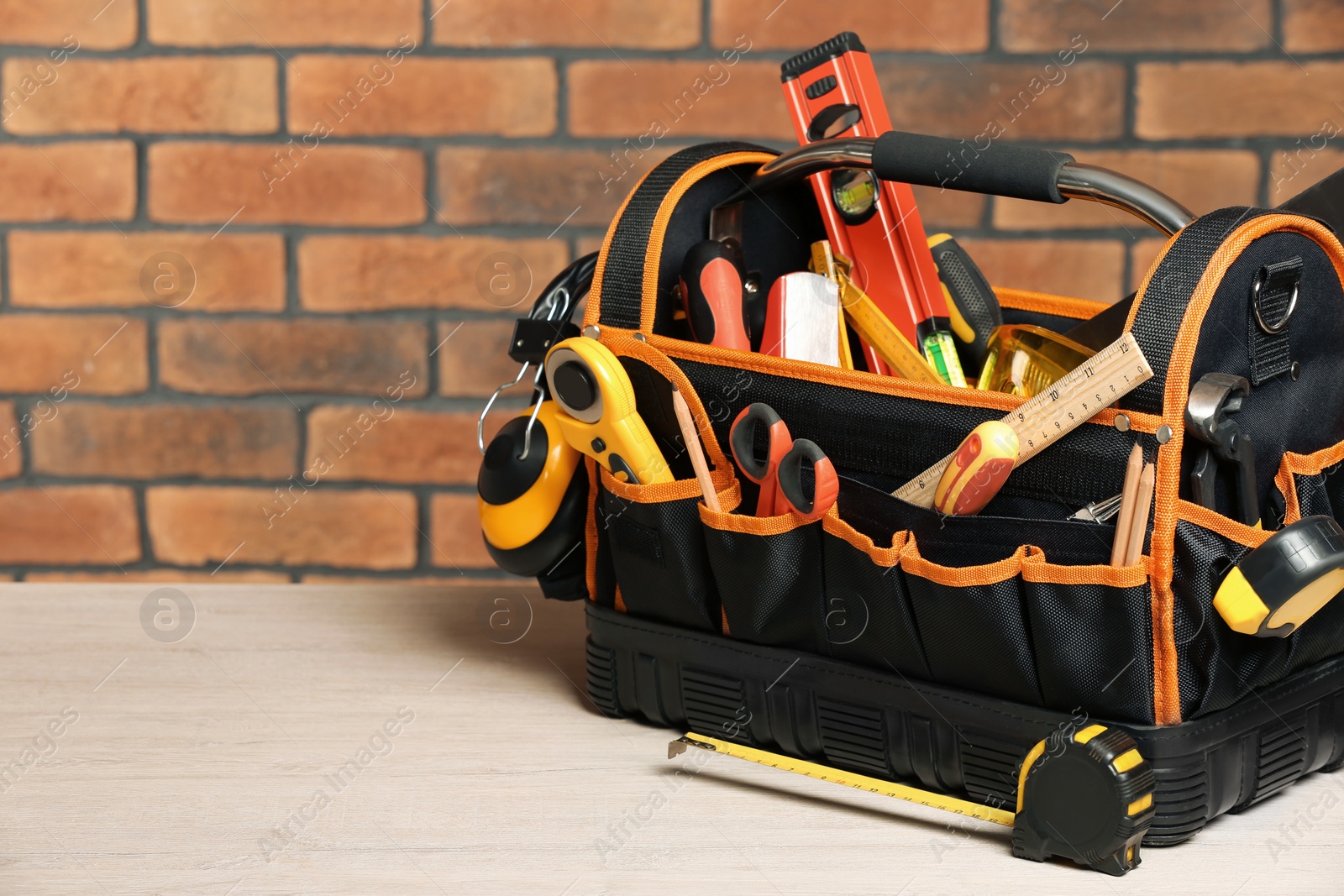 Photo of Bag with different tools for repair on white wooden table near brick wall. Space for text