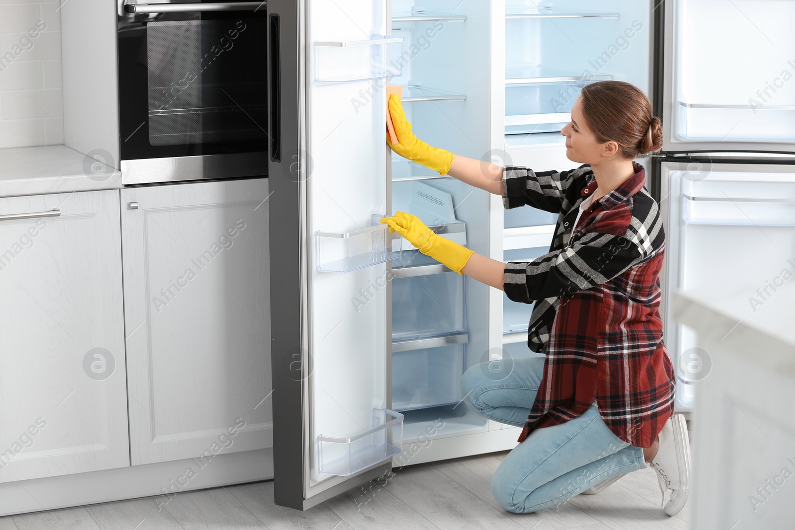 Photo of Woman in rubber gloves cleaning refrigerator at home