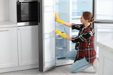 Photo of Woman in rubber gloves cleaning refrigerator at home