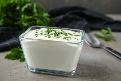 Photo of Glass bowl of fresh sour cream with parsley on grey table