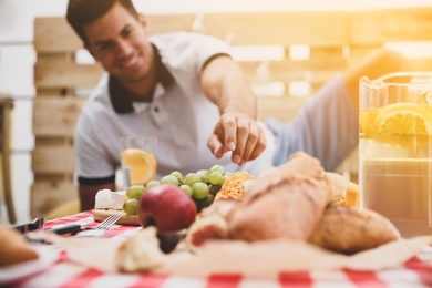 Man with tasty food and drink imitating picnic at home