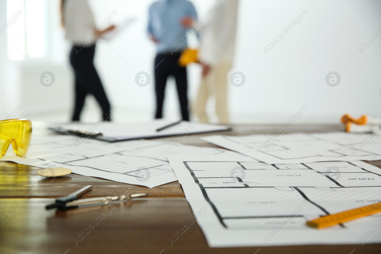 Photo of Colleagues in office, focus on table with construction drawings and tools