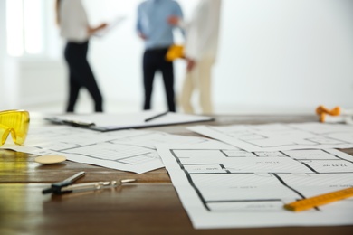 Photo of Colleagues in office, focus on table with construction drawings and tools