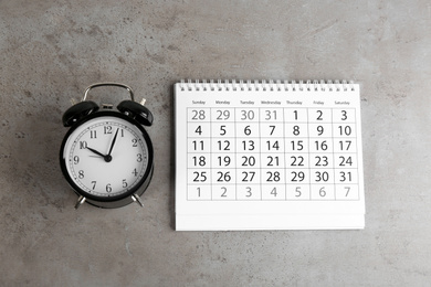 Calendar and alarm clock on grey stone background, flat lay