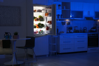 Photo of Stylish kitchen interior with refrigerator full of products at night