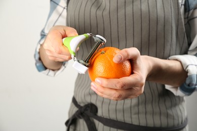 Photo of Woman peeling fresh orange on light grey background, closeup