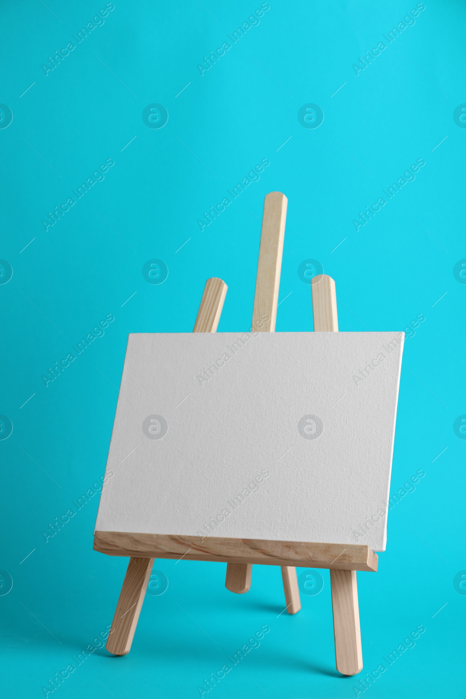 Photo of Wooden easel with blank canvas board on color background. Children's painting