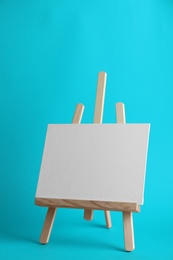 Photo of Wooden easel with blank canvas board on color background. Children's painting