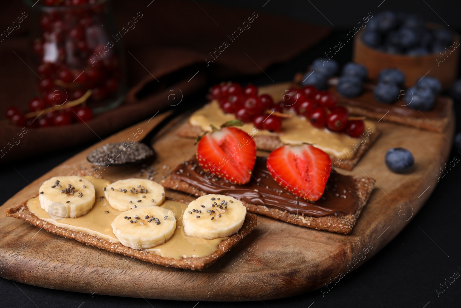 Photo of Fresh crunchy rye crispbreads with different toppings on black table, closeup