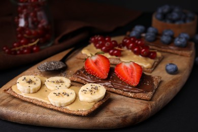Photo of Fresh crunchy rye crispbreads with different toppings on black table, closeup