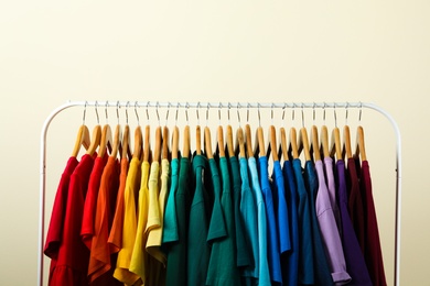 Rack with bright clothes on light background. Rainbow colors